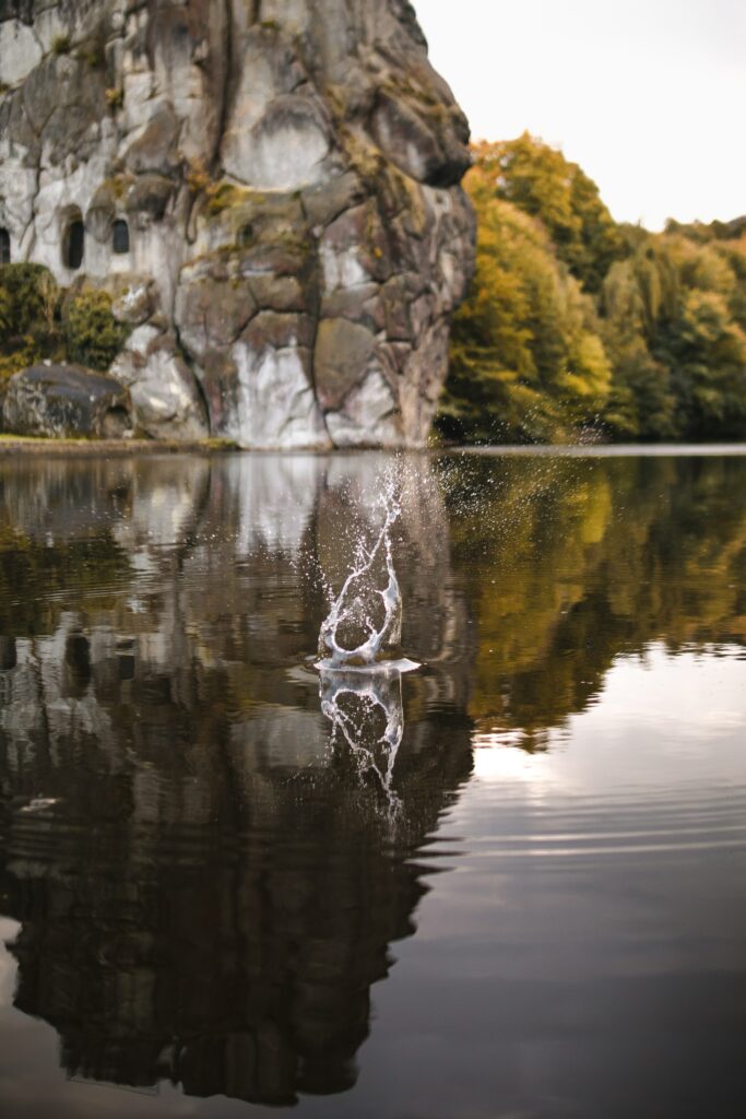 Tranquil lake splash with autumn trees and rugged cliffs reflected in serene natural wallpaper