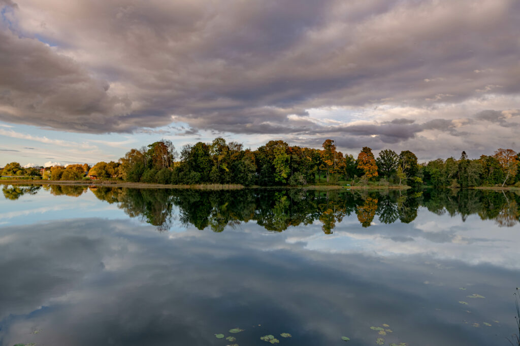 Tranquil lake with lush tree reflections under dramatic cloud-filled sky serene wallpaper background