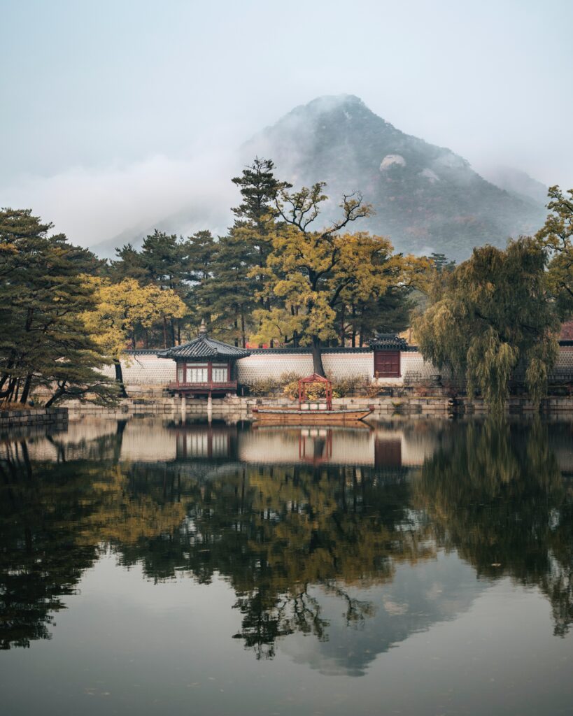 Tranquil lakeside gazebo surrounded by lush trees misty mountains reflected in calm water wallpaper