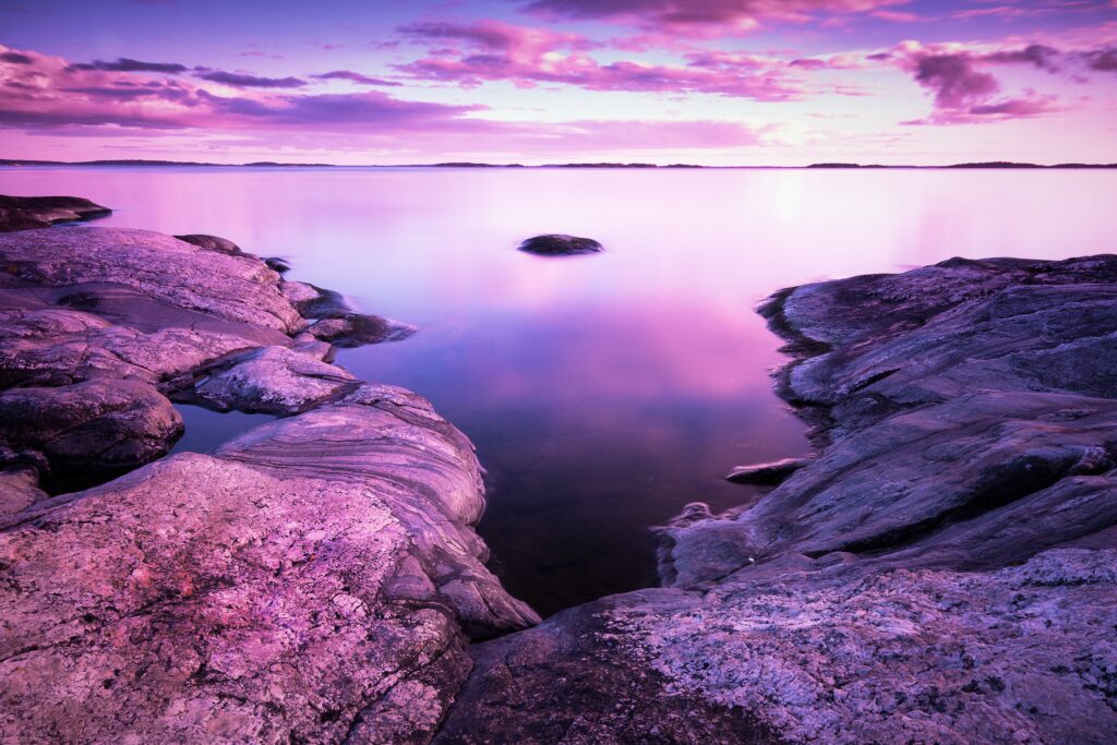 Serene lakeside wallpaper with smooth stones rugged rocks calm water and purple sky reflection