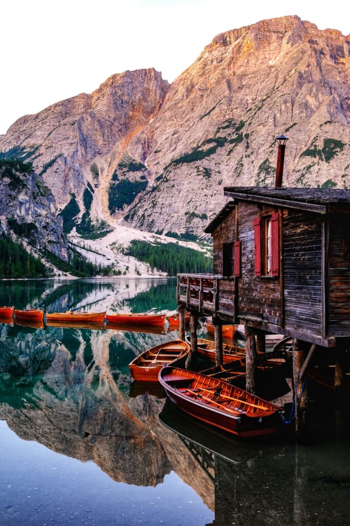 Vibrant wooden boats tied to rustic pier by lake with mountain reflections in calm clear water Wallpaper
