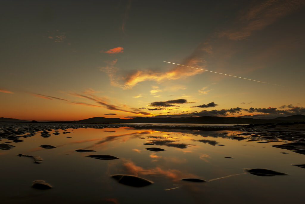 Sunset lakeside scene with warm orange hues and tranquil mirrored reflection on still water Wallpaper