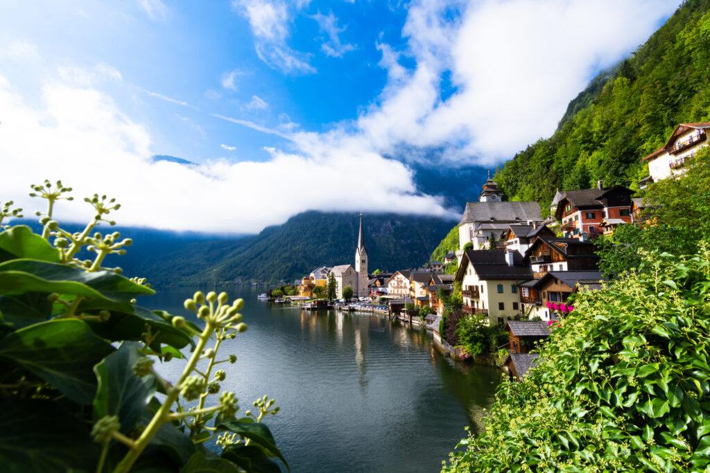 Tranquil lakeside village with church steeple reflecting on calm water and mountain backdrop Wallpaper