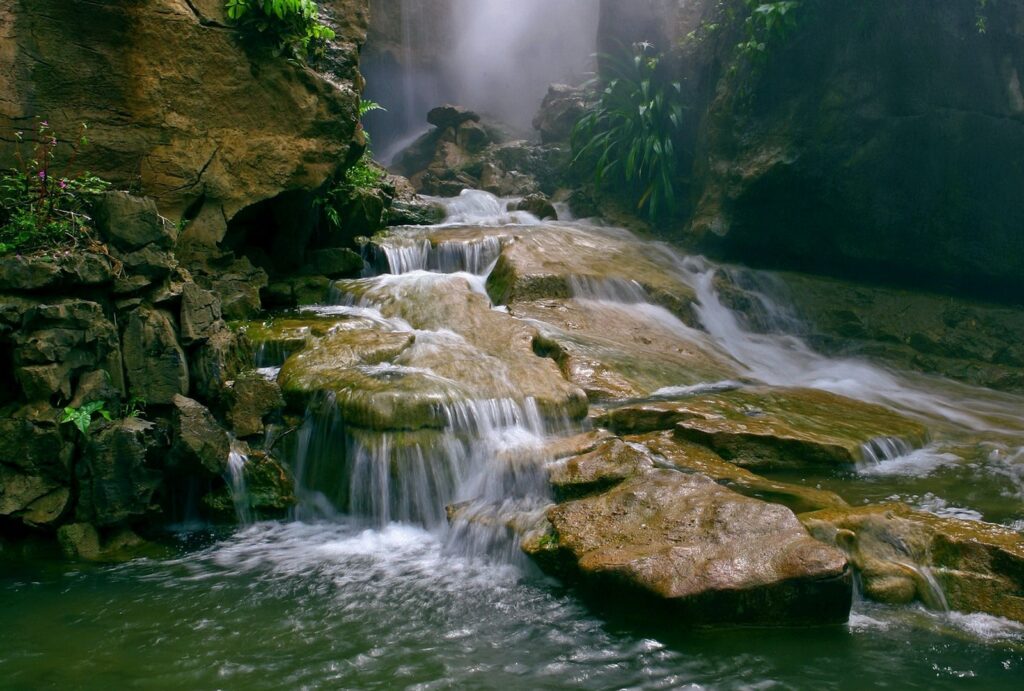 Serene wallpaper with layered stone waterfalls flowing into a clear stream surrounded by greenery