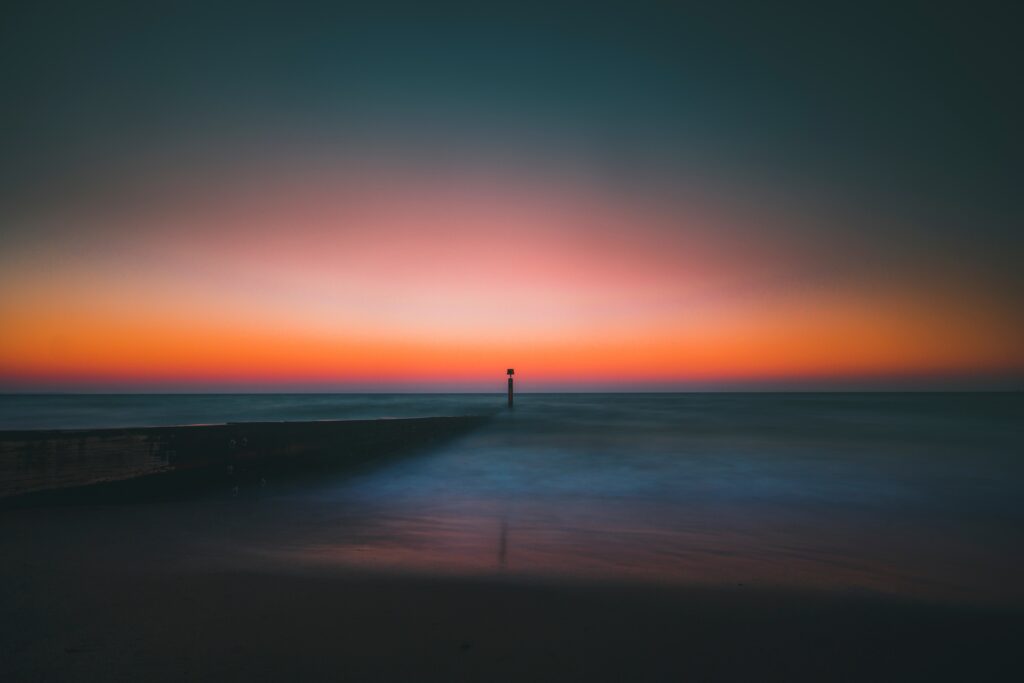 Lighthouse at pier over calm sea with gradient blue to orange sky serene peaceful wallpaper background