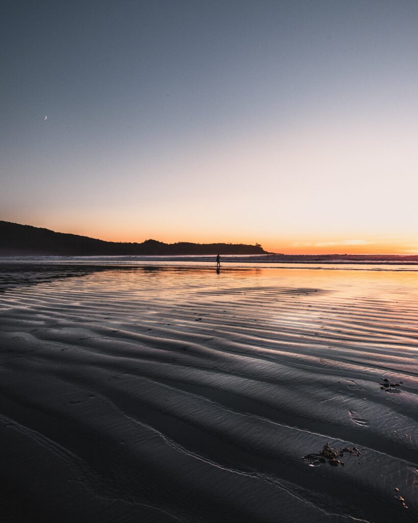 Serene ocean at low tide with gentle sand ripples lone silhouette sunset horizon wallpaper background