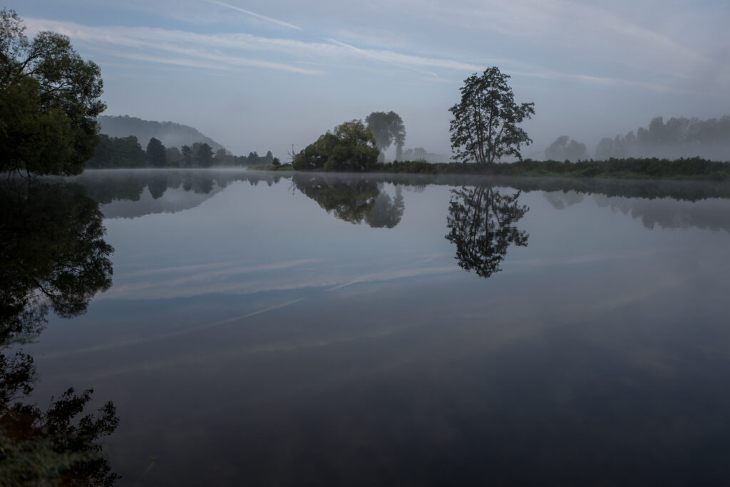 Tranquil river reflecting tree silhouettes and misty landscape under early dim sky wallpaper background