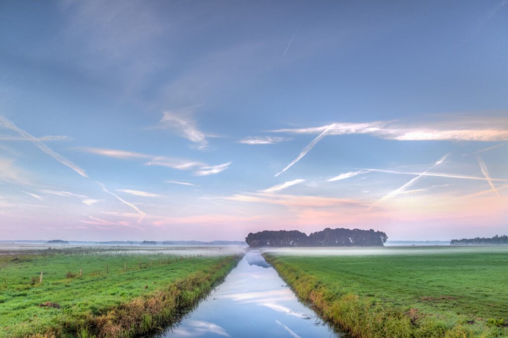 Tranquil morning fog over green fields with reflective canal and pastel sky rural landscape wallpaper