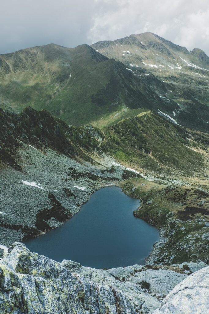 Aerial view of tranquil mountain lake surrounded by rugged rocks lush green slopes and snowy peaks Wallpaper