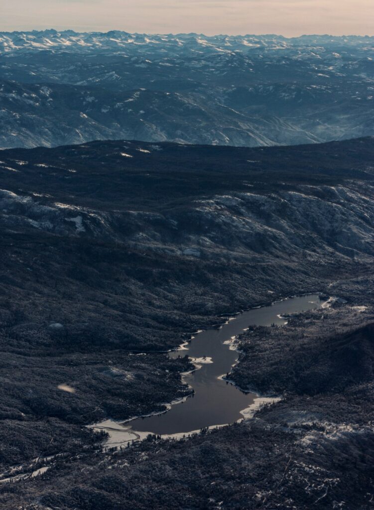 Aerial view of tranquil lake in forested valley surrounded by majestic mountain peaks at dawn Wallpaper