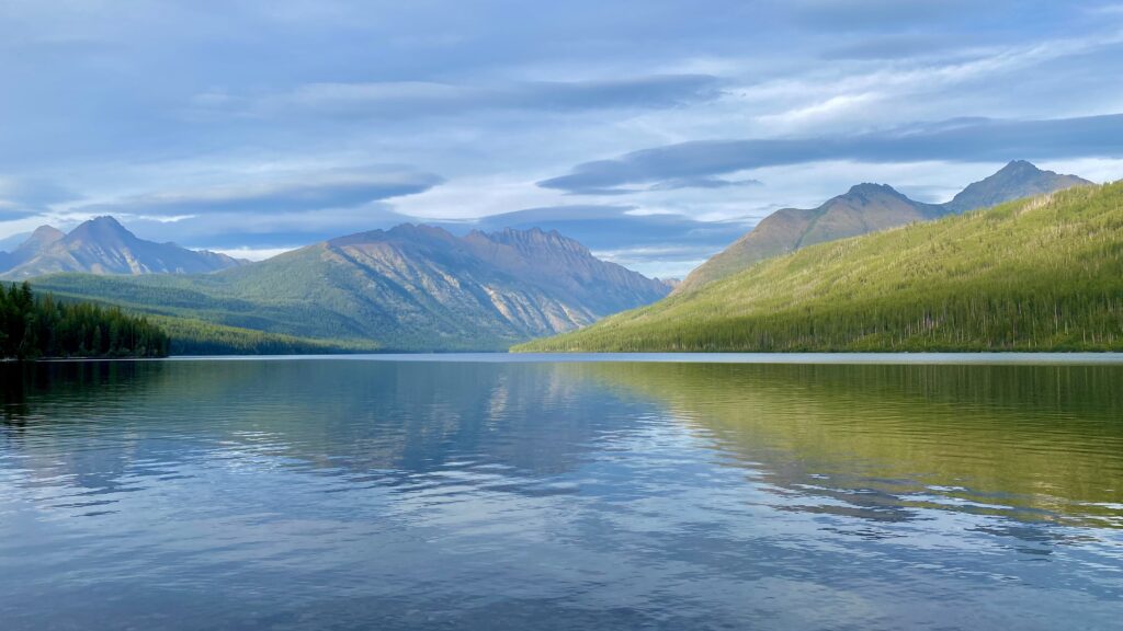 Tranquil lake with clear reflections surrounded by lush forests and towering mountain peaks Wallpaper