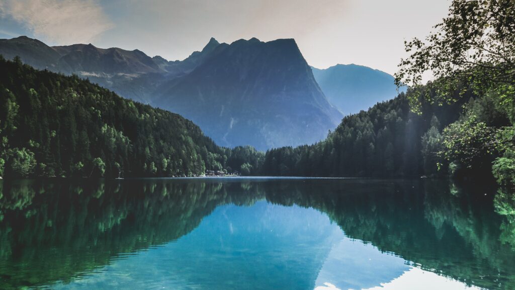 Tranquil mountain lake with dense green forests and majestic peaks reflecting in still water wallpaper