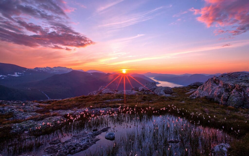 Sunset over tranquil lake with rugged rocks and distant mountains peaceful landscape wallpaper
