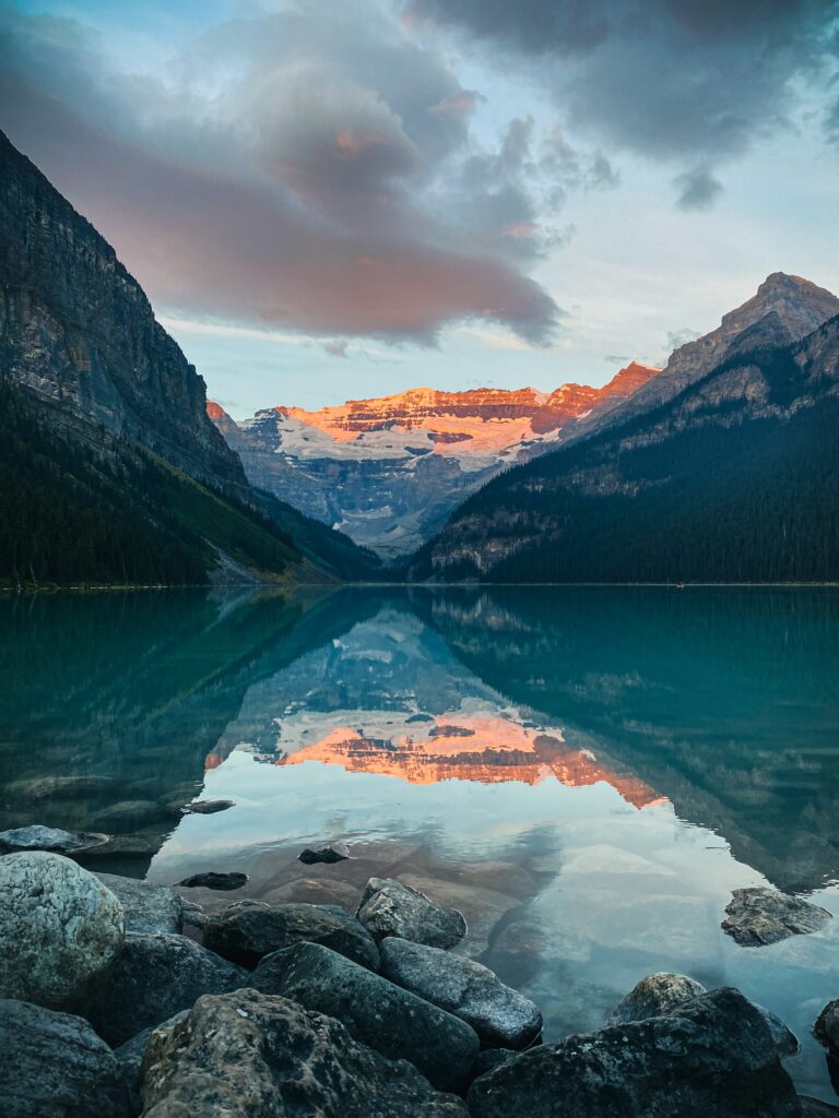 Mountain lake sunset with smooth stones and majestic reflected slopes in calm glassy water Wallpaper