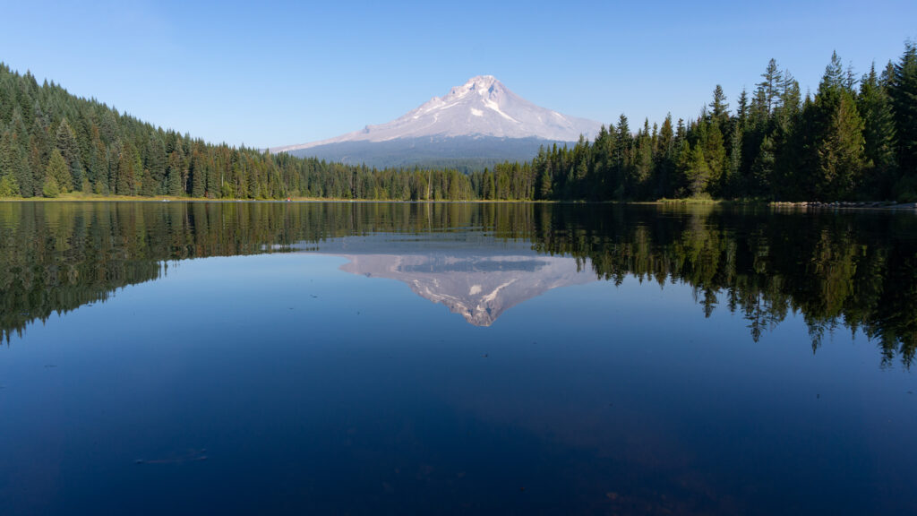 Tranquil mountain lake reflecting snow-capped peak and dense green forest in vibrant nature Wallpaper