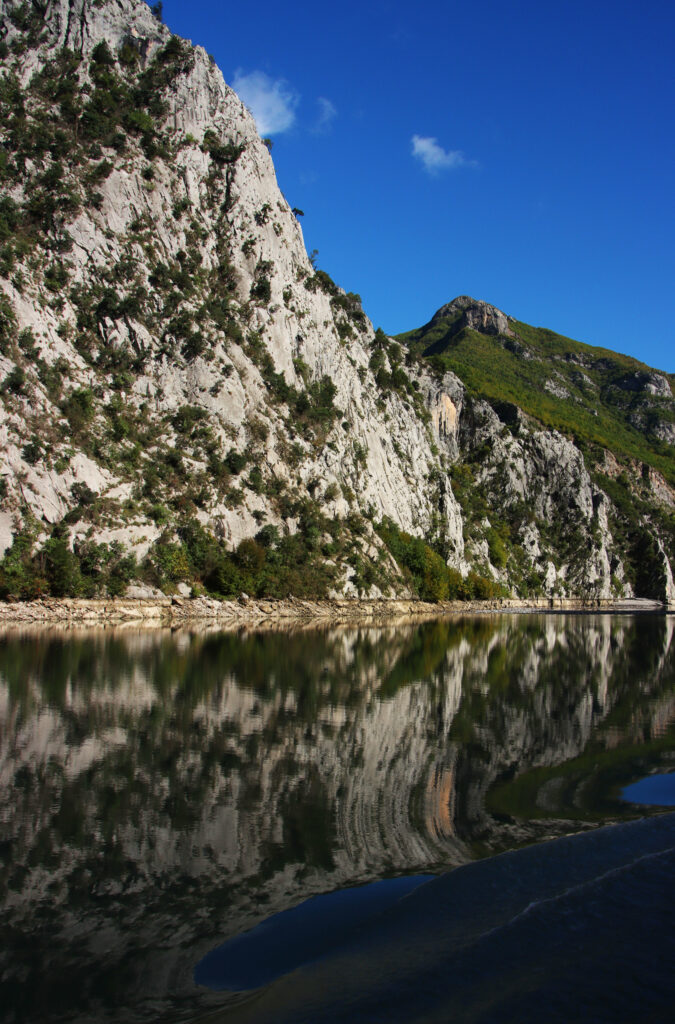 Mountain landscape wallpaper with rugged cliffs and clear lake reflecting blue sky and waves