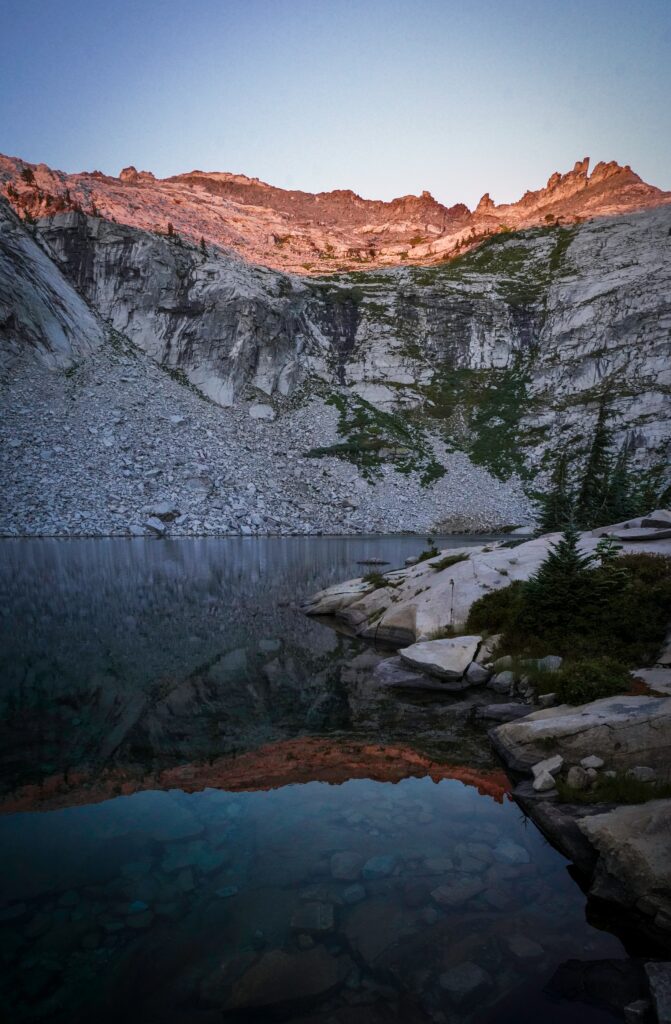 Tranquil lake with clear water stones surrounded by rugged rocks and glowing mountain peaks Wallpaper