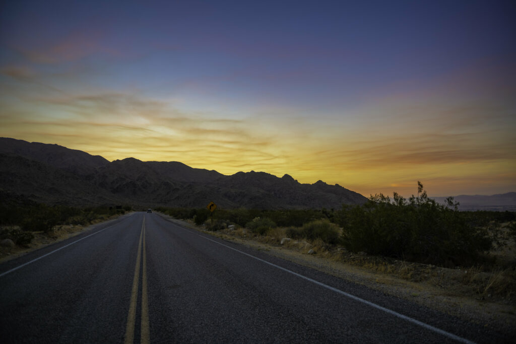 Tranquil desert road with rugged mountains under vibrant orange and blue sunset sky landscape Wallpaper