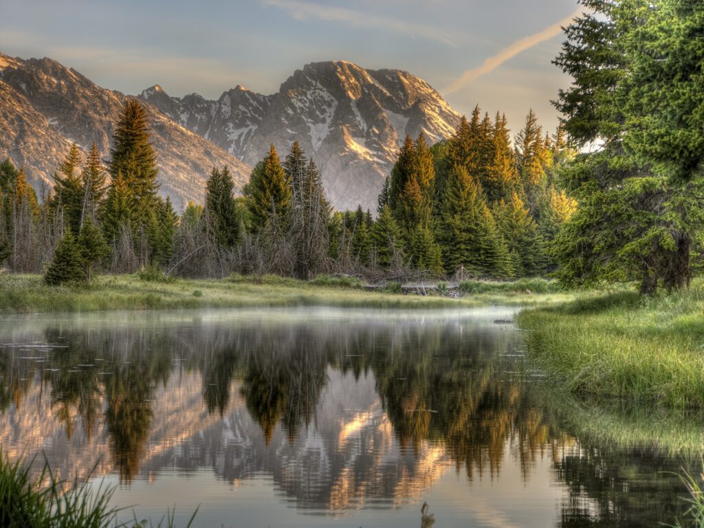 Serene mountain sunrise with fog lush green trees and calm lake reflecting colorful sky wallpaper