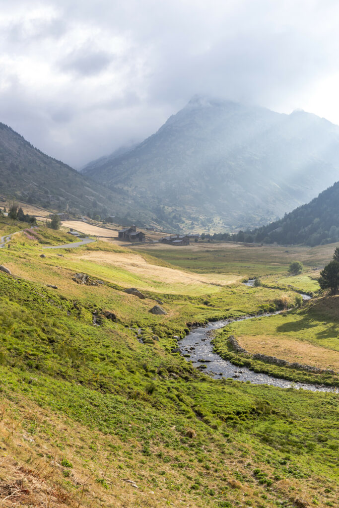 Tranquil valley with winding stream lush green grass majestic mountains soft clouds sunlight Wallpaper