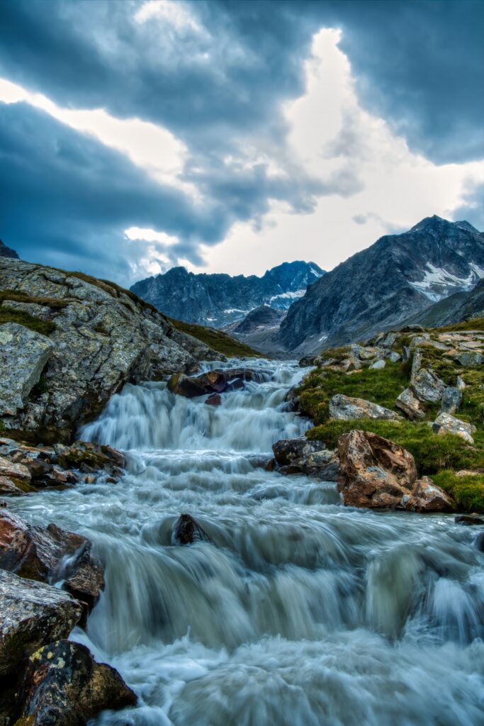Waterfall cascading over rocky stones in lush green mountains under dramatic cloudy sky wallpaper