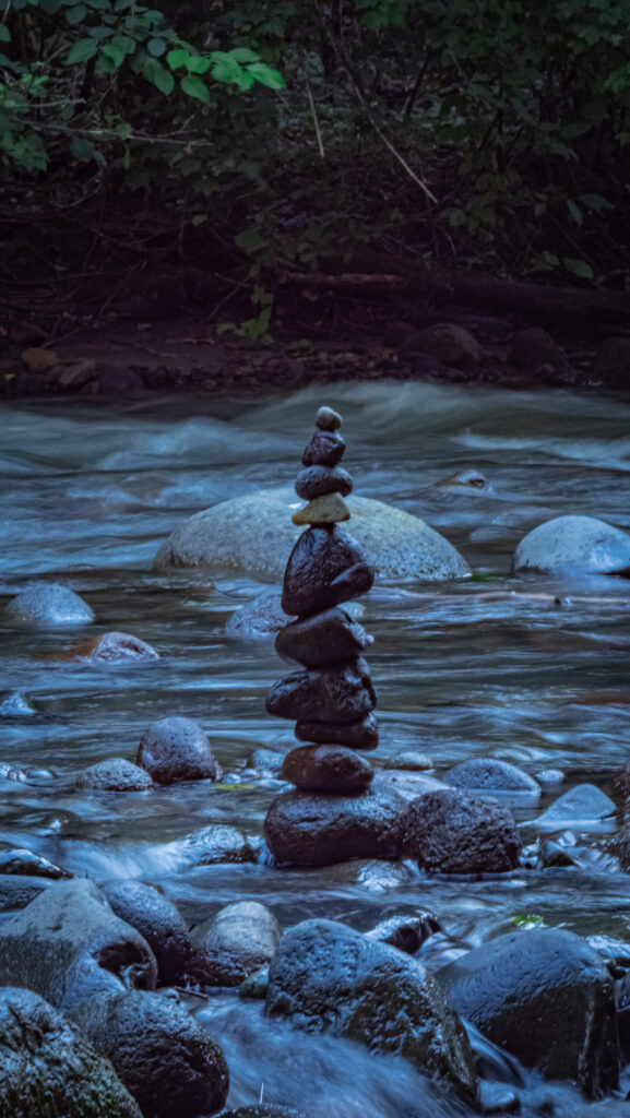 Balanced smooth stones in a flowing stream surrounded by lush greenery serene nature wallpaper