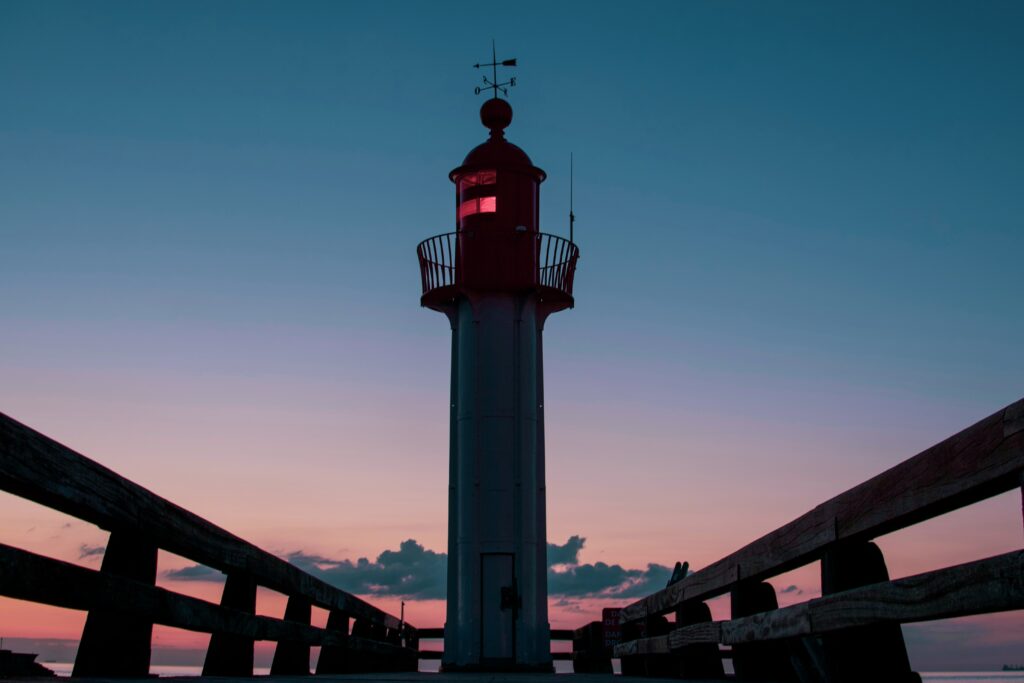 Lighthouse silhouette at twilight with wooden railings under deep blue and pink coastal sky background Wallpaper