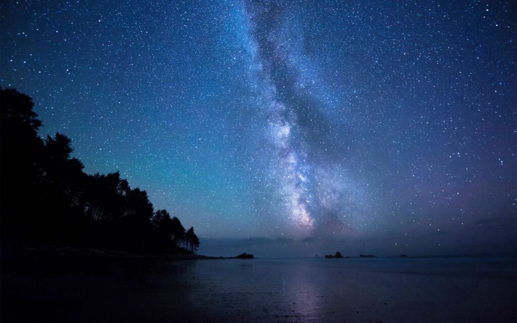 Serene shore under starry night sky with glowing Milky Way in blue violet hues wallpaper