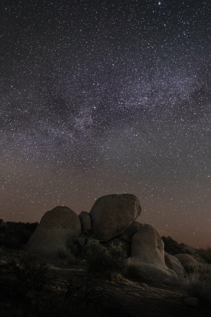 Tranquil night sky with large stone formations and bright stars illuminating rocky terrain wallpaper