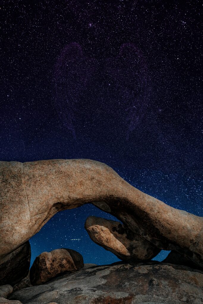 Serene night sky with twinkling stars over rugged natural rock arch in deep blue purple hues wallpaper