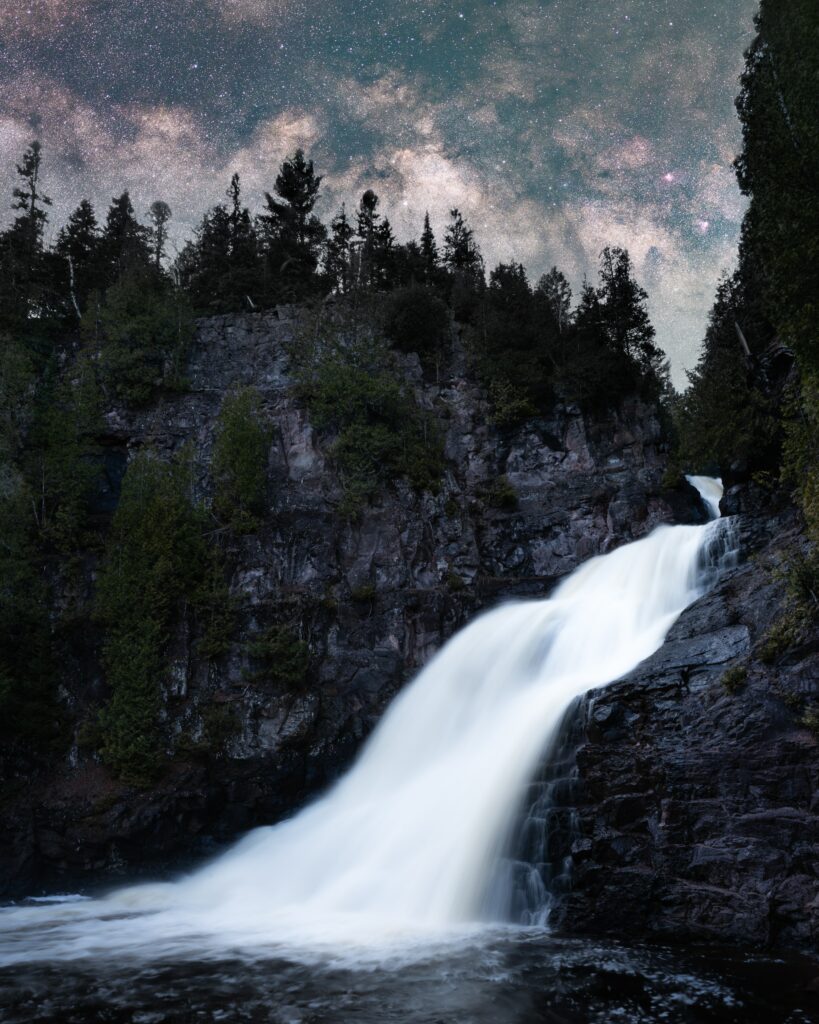 Night waterfall over rugged rocks surrounded by dense forest under a starry sky wallpaper background
