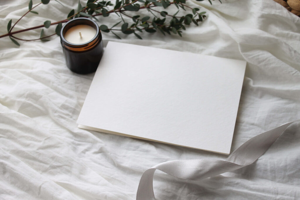 Tranquility in White: A Delicate Candle and Plant Branch Rest on Plain White Paper Sheets Wallpaper