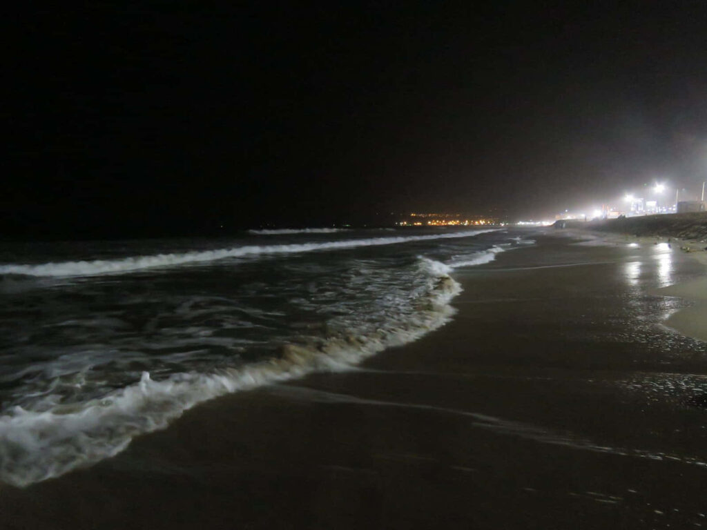 Tranquil Nighttime Beach: Lights Reflecting on Gentle Waves Wallpaper