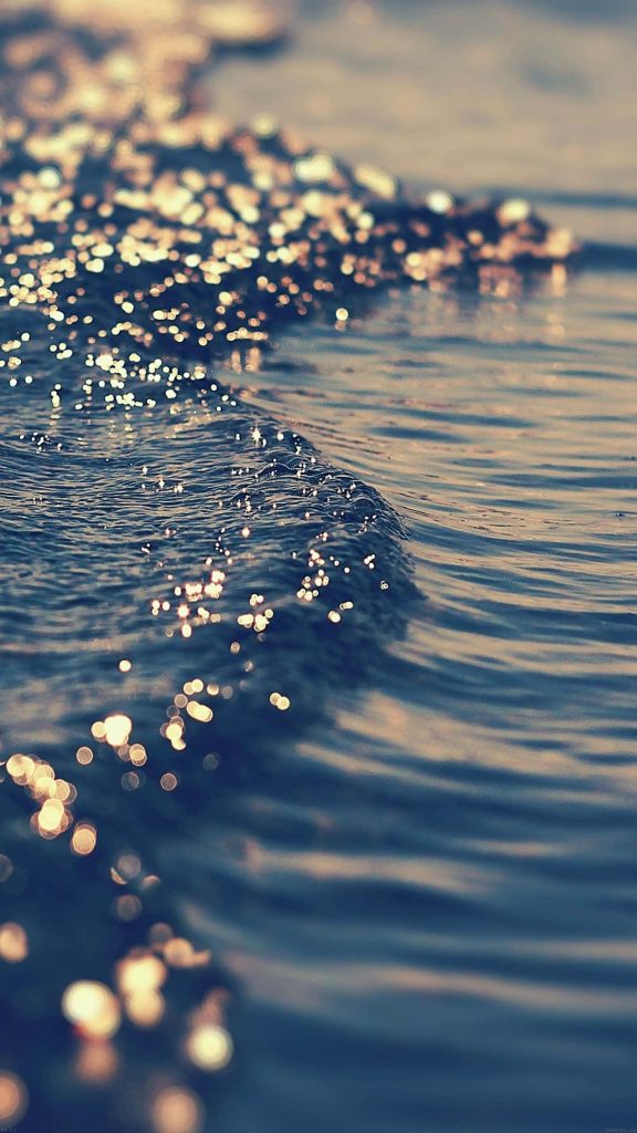 Serene deep blue ocean surface with golden sunlight ripples and soft bokeh effect wallpaper