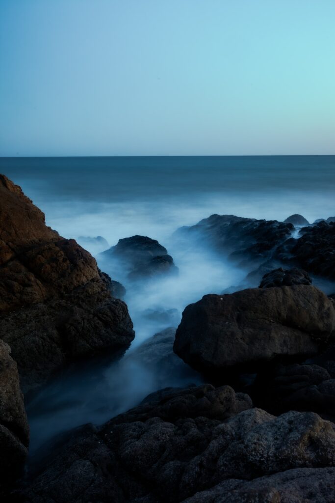 Tranquil ocean at dusk with misty waves and rugged rocks serene landscape wallpaper background
