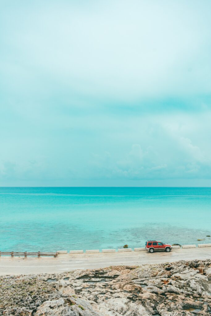 Tranquil ocean turquoise water horizon rugged coast red modern vehicle roadside wallpaper background