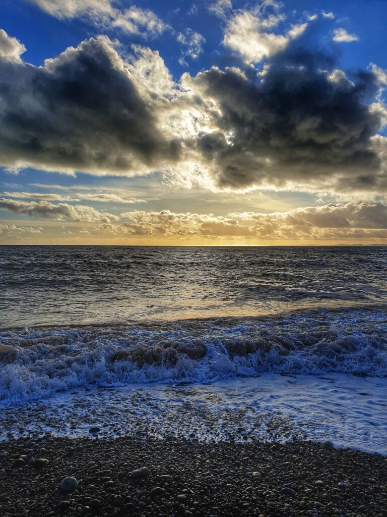 Tranquil pebble beach with gentle waves and dramatic cloudy sky at golden hour wallpaper background