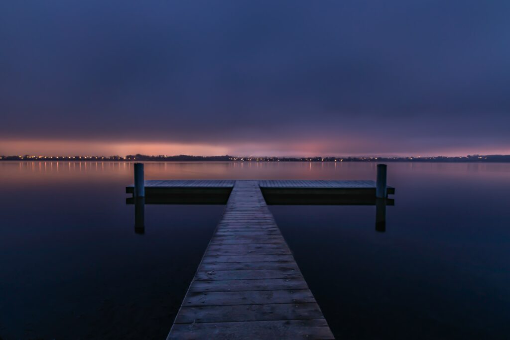 Tranquil pier over calm water at sunset with dramatic night sky blending blues and purples Wallpaper