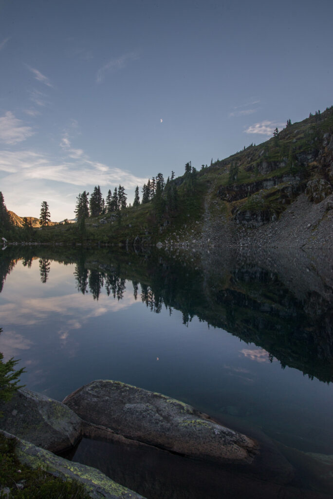 Serene pond with clear reflections lush trees rugged stones peaceful nature wallpaper background