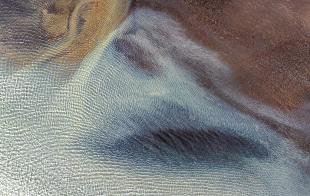 Aerial view of tranquil river with soft ripples and earthy brown blue textured shore wallpaper