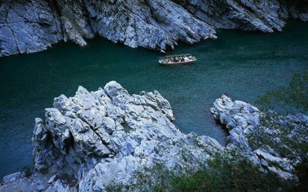 Tranquil river flowing between rugged gray cliffs with wooden boat on emerald waters wallpaper