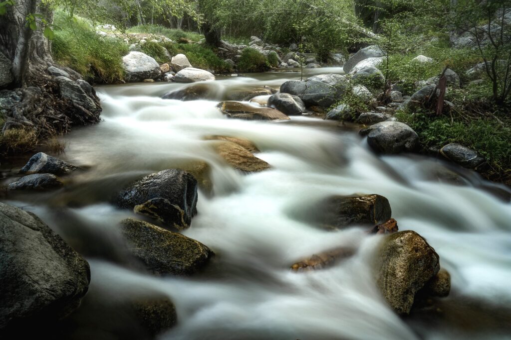 Tranquil river flowing over smooth stones in lush green landscape with soft misty water effect Wallpaper