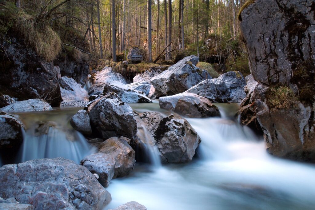 Tranquil river flowing over smooth rocks surrounded by dense forest and lush greenery wallpaper