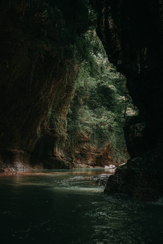 Tranquil river flowing between dark rocky cliffs with lush greenery and soft reflections wallpaper