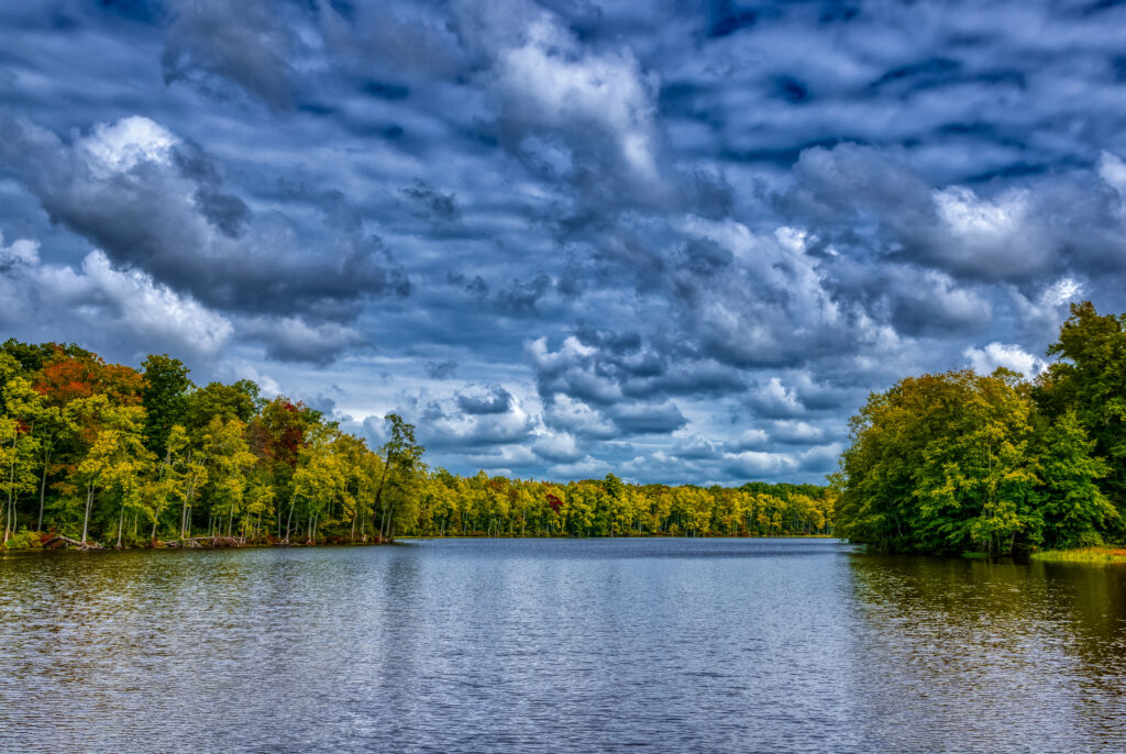 Tranquil river with lush green and gold trees under swirling dramatic sky landscape wallpaper