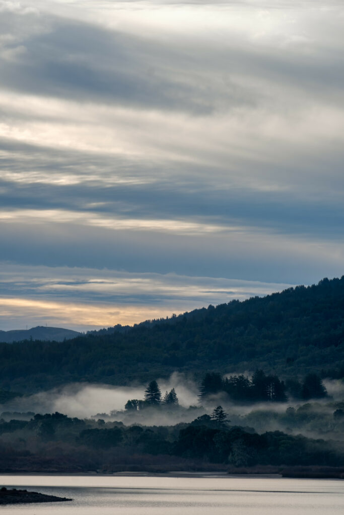 Serene landscape wallpaper with calm river lush forest mountains and morning fog under soft clouds