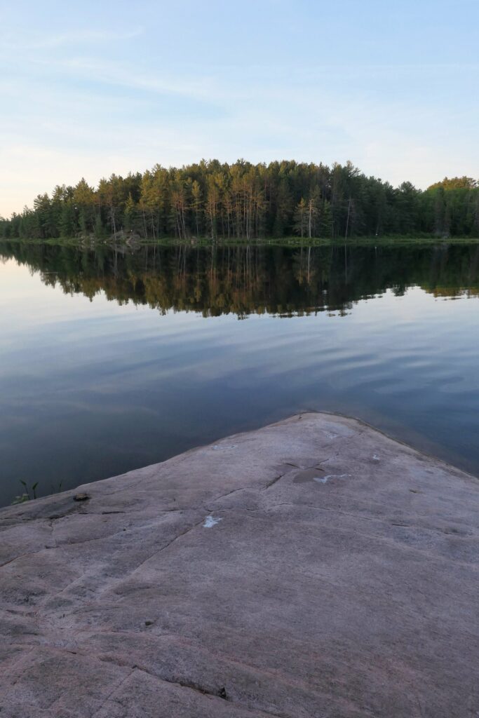 Serene river with dense spruce forest reflected in calm water and smooth stone foreground wallpaper
