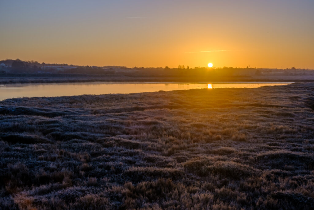 Tranquil river winding along rugged coast at sunset with golden hues reflecting on calm water Wallpaper