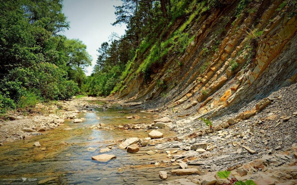 Tranquil river winding through lush green valley with sharp mountain ridges and rocky slopes Wallpaper