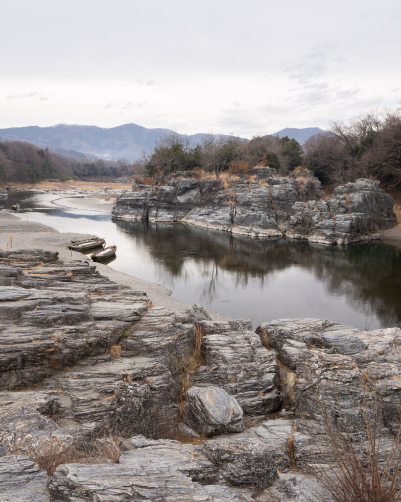 Tranquil river winding through rugged rocks and sparse bushes under cloudy sky with distant mountains Wallpaper